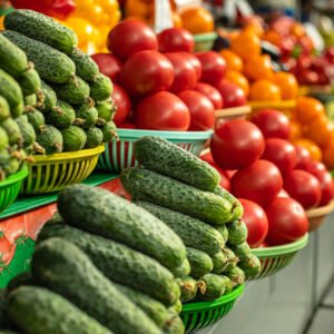 View over fresh organic cucumbers and tomatoes in sorted in baskets on the counter at the market. Raw veggies at the market.